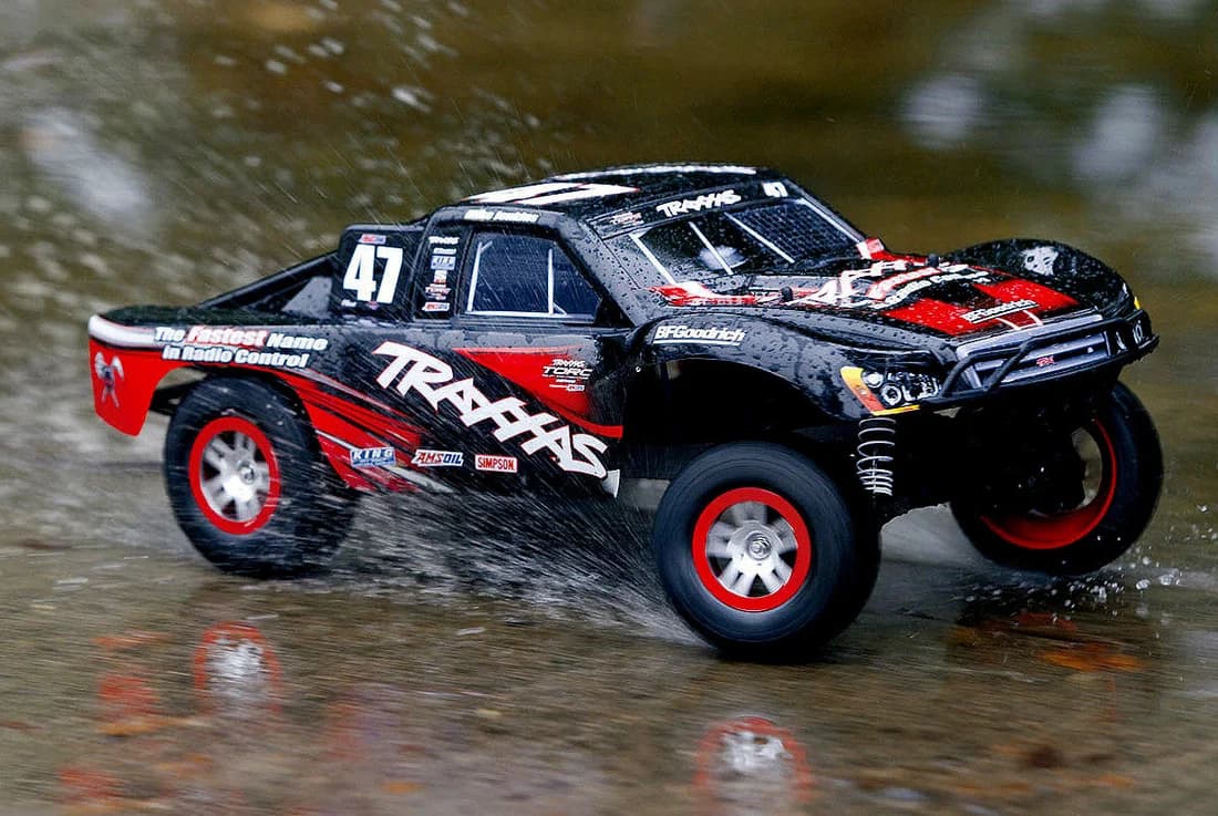 Black and red Traxxas RC truck splashing through a puddle, spraying water into the air.
